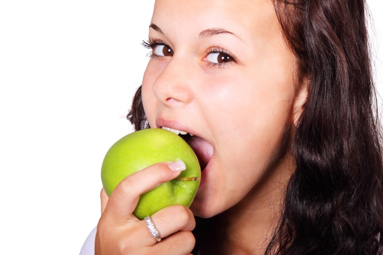 Girl taking bite out of green apple